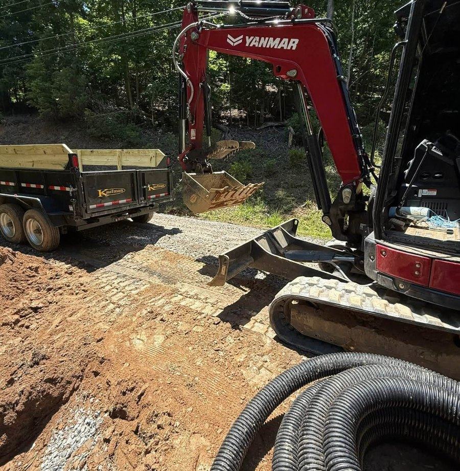 Corrugated drainage pipe staged beside an excavator on a drainage job.