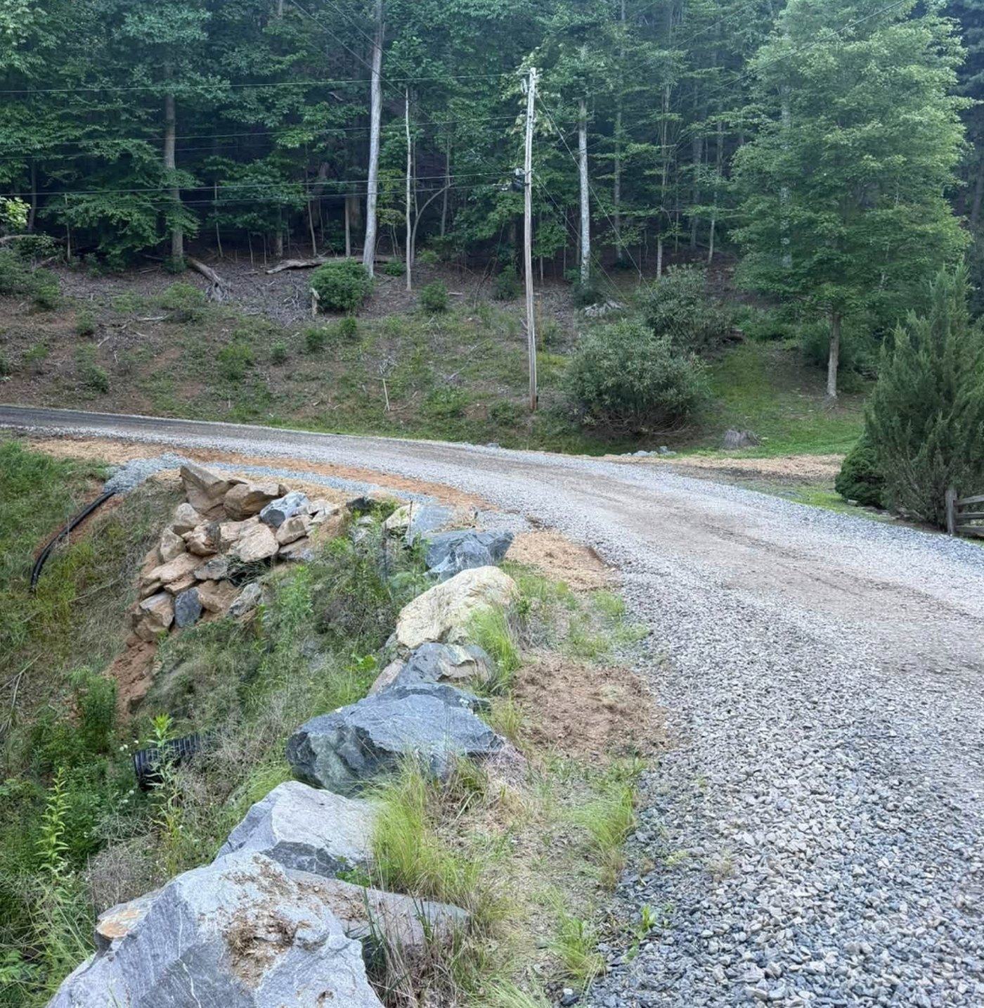 A gravel driveway cut into grade with a shaped stone ditch line running alongside it.