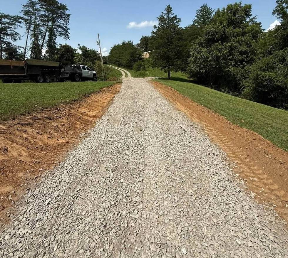 A long finished gravel driveway running between mown verges to a wooded property in Western North Carolina.