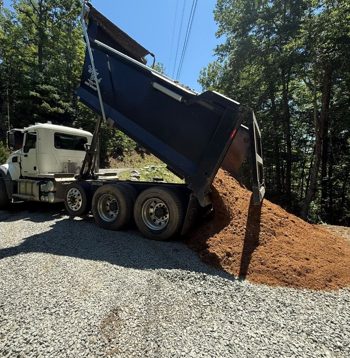 A dump truck placing a load of gravel on a new driveway base.