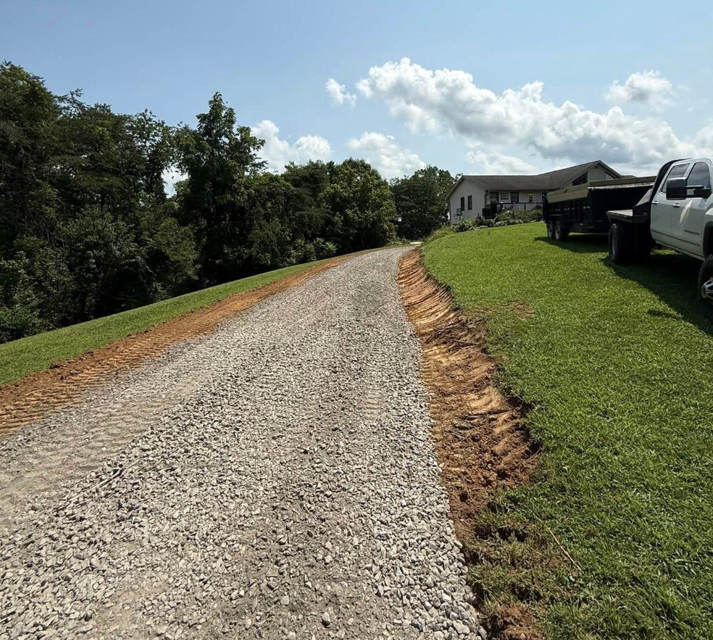 A finished gravel driveway curving uphill to a residence.