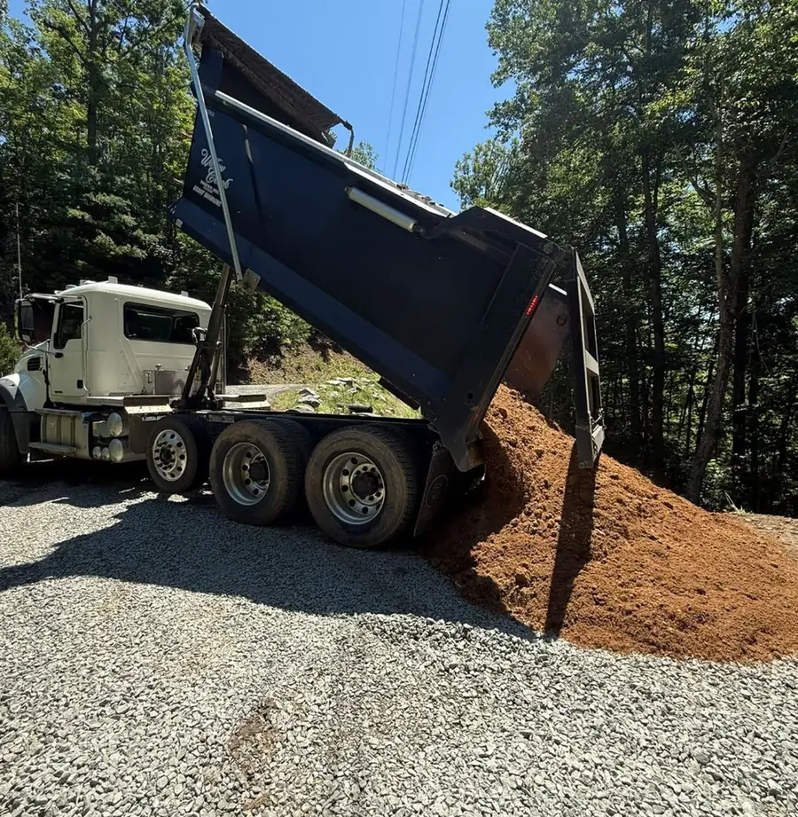 A dump truck placing a load of gravel on a new driveway base.