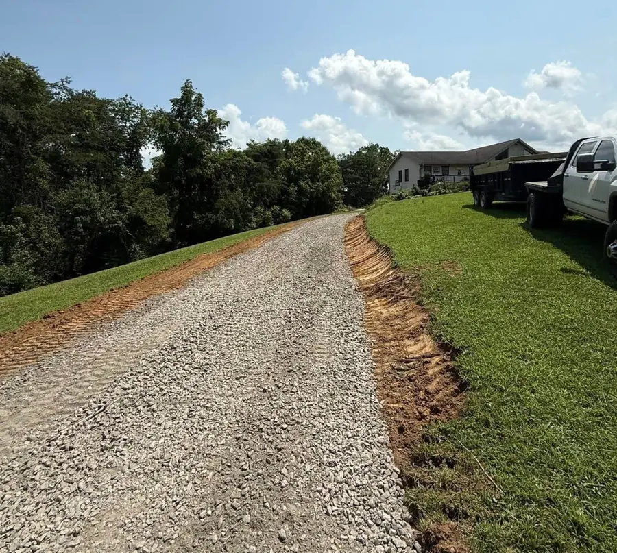 A finished gravel driveway curving uphill to a residence.