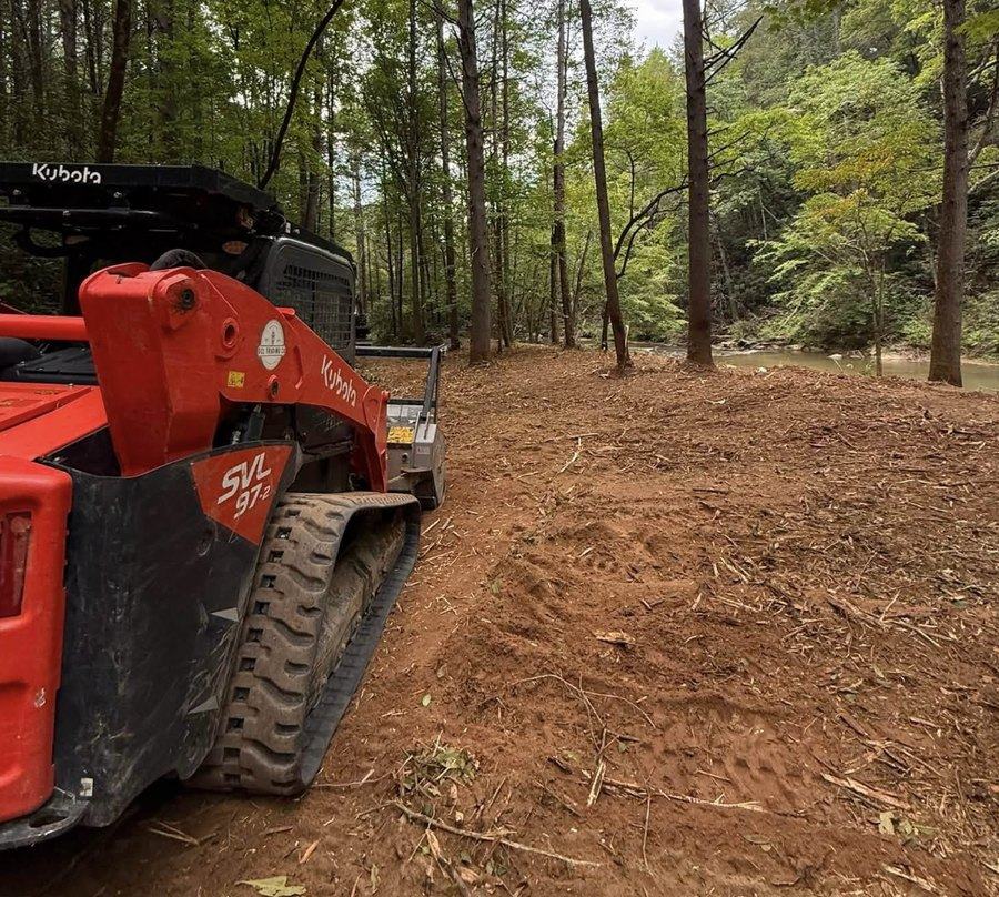 A tracked skid steer with a mulching head clearing woodland.